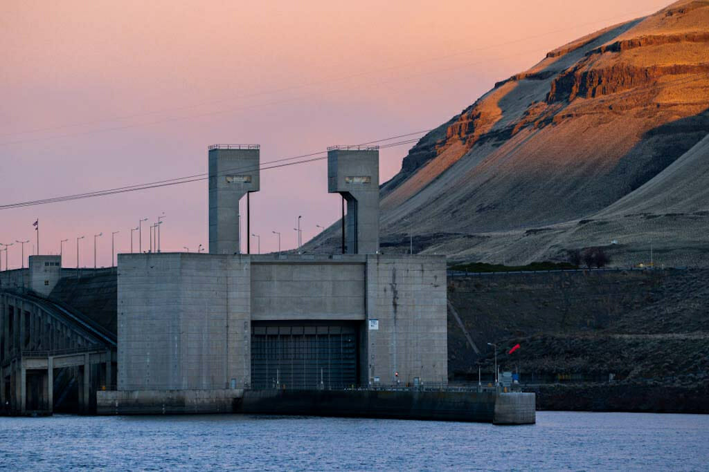 A dam with a sunset sky behind it and a mountain
